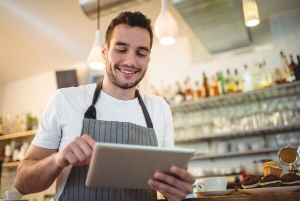Read Our Reviews - Closeup View of a Smiling Young Barista Holding a Laptop While Standing in a Coffee Shop